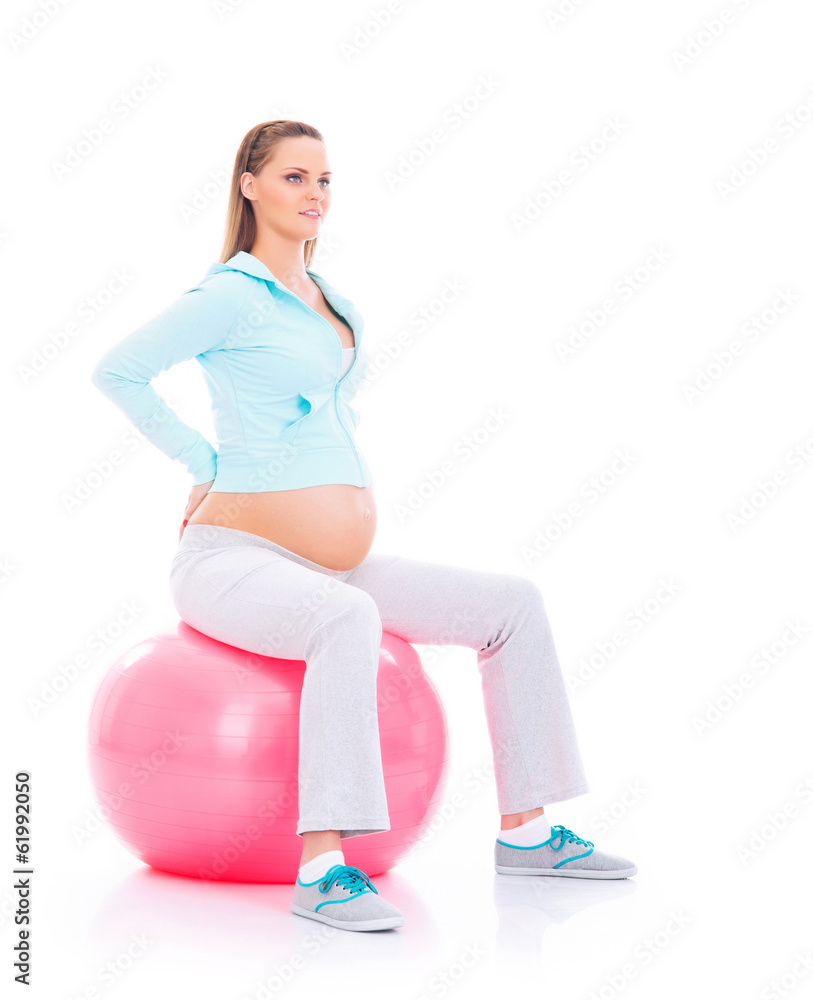 A young pregnant woman working out with a fitness ball
