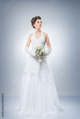 A beautiful bride with a flower bouquet on grey