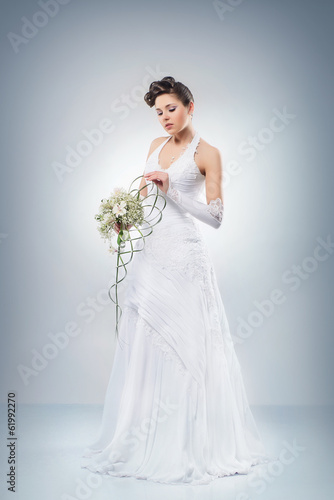 A bride standing with a flower bouquet on grey