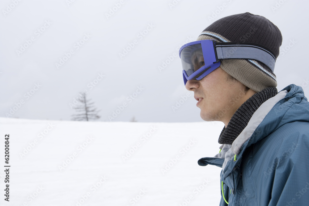profile of man wearing goggles and standing still in snowy field profile of man wearing goggles and standing still in snowy field