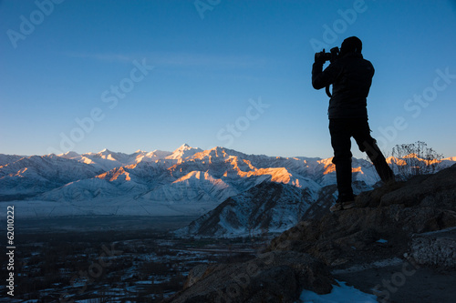 Silhouette of traveler taking photo of sunrise over mountain.