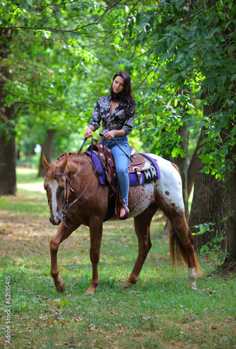 Young beautiful cowgirl with horse in forest