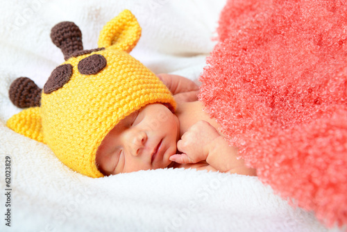 cute baby sleeping in funny yellow giraffe hat and smiling in sw © Khorzhevska