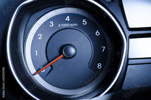 Car tachometer with red arrow.