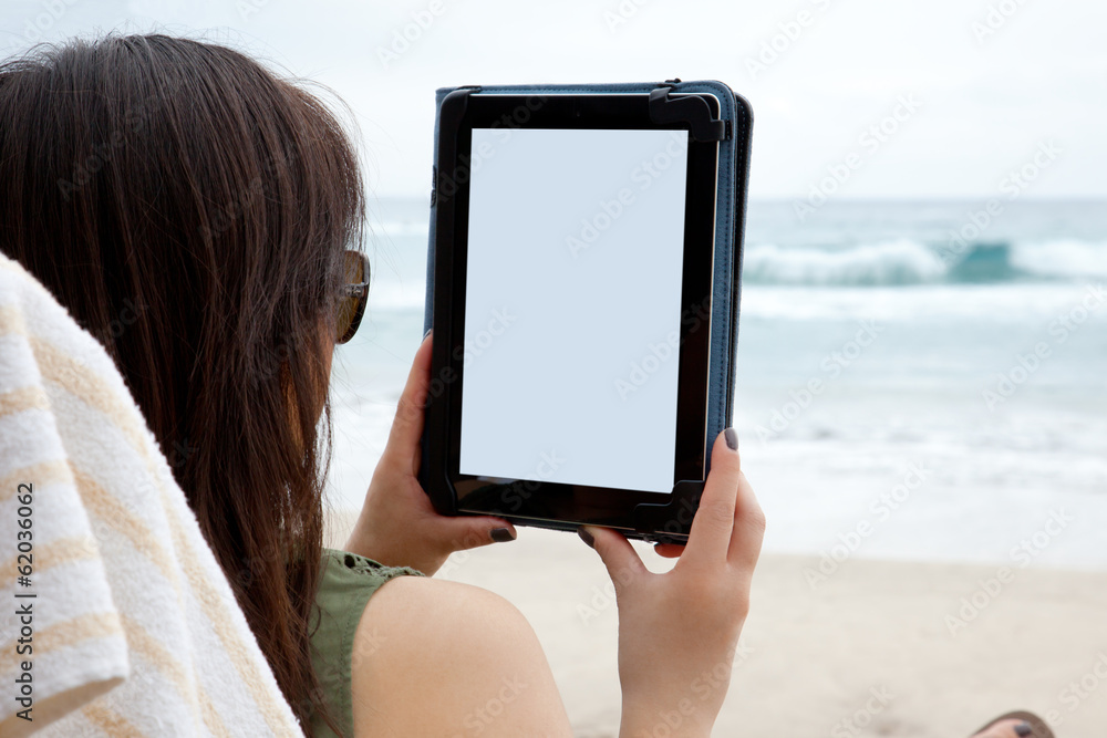 A woman uses a tablet device while on the beach.