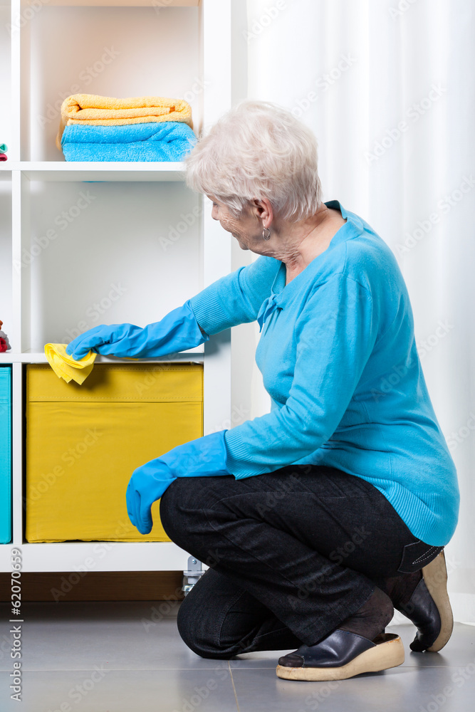 Elderly woman during dusting furniture