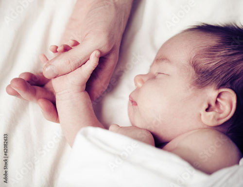 Newborn baby and his father's hand - care and safety concept