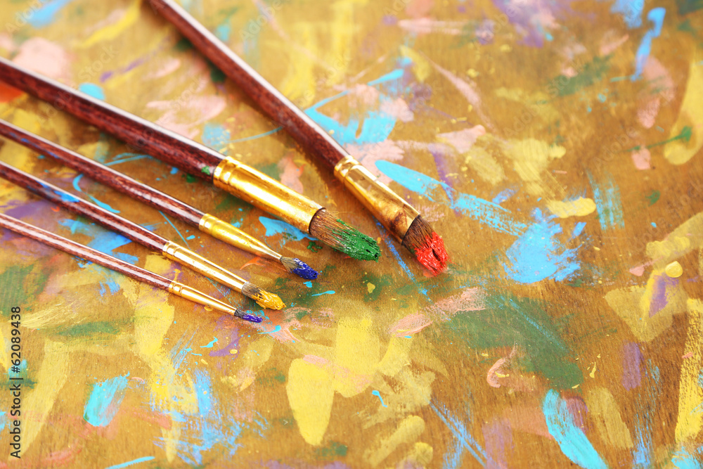 Fototapeta premium Many brushes in paints on multicolor wooden background