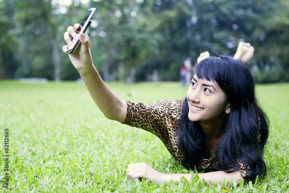 Asian woman taking picture with mobile phone at the park