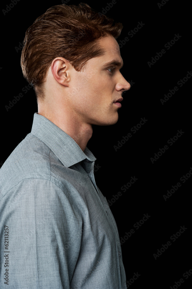 side view of a casual young man standing with a hand in his pocket and with