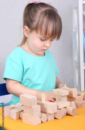 Little girl plays with construction blocks sitting at table in