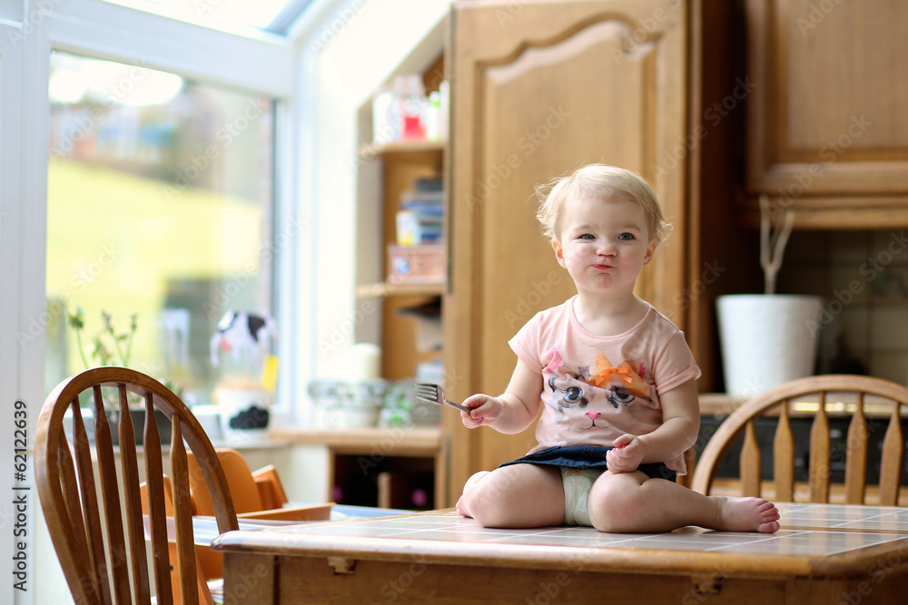 toddler girl eating something with fork sitting on the table