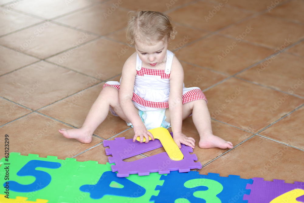 Fototapeta premium Happy toddler girl playing with colorful numbers puzzles