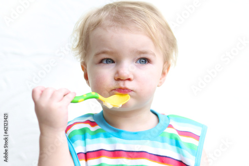 sweet blonde toddler girl wearing colorful bib eating porridge
