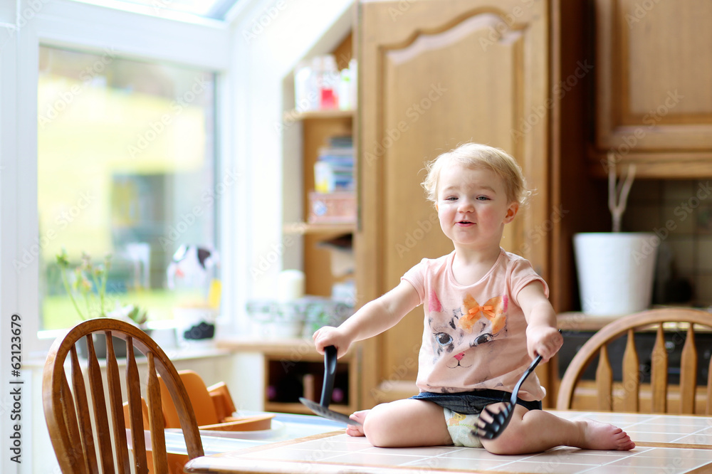 toddler girl playing with ladle and skimmer sitting on the table