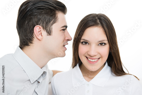 Portrait of young man telling a secret to a woman over a white background