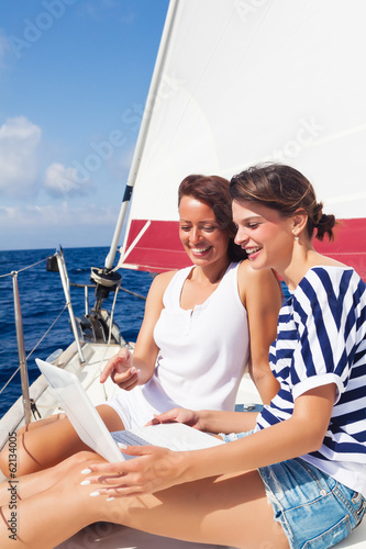 Happy women on the bow of a Sailboat using a laptop © Avatar_023