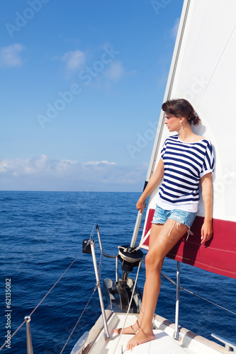 Beautiful young woman standing on the bow of a Sailboat, looking away. Copy space