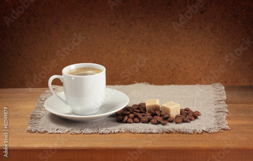 Coffee cup, saucer, sugar, napkin on wooden table.