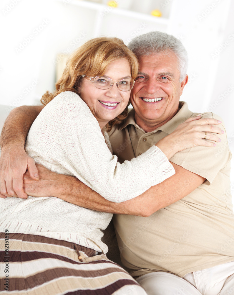 Hugging Senior couple sitting in living room. Hugging Senior couple sitting in living room.