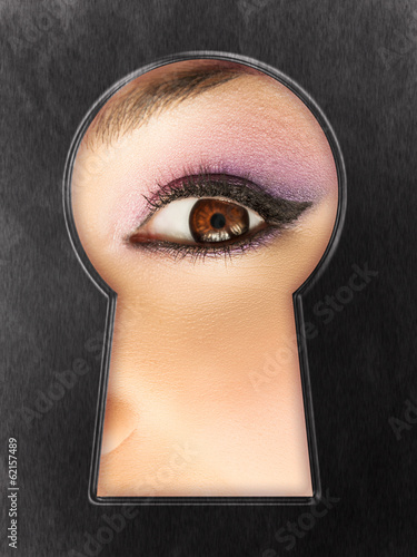 Female curiosity - woman eye looking through the keyhole