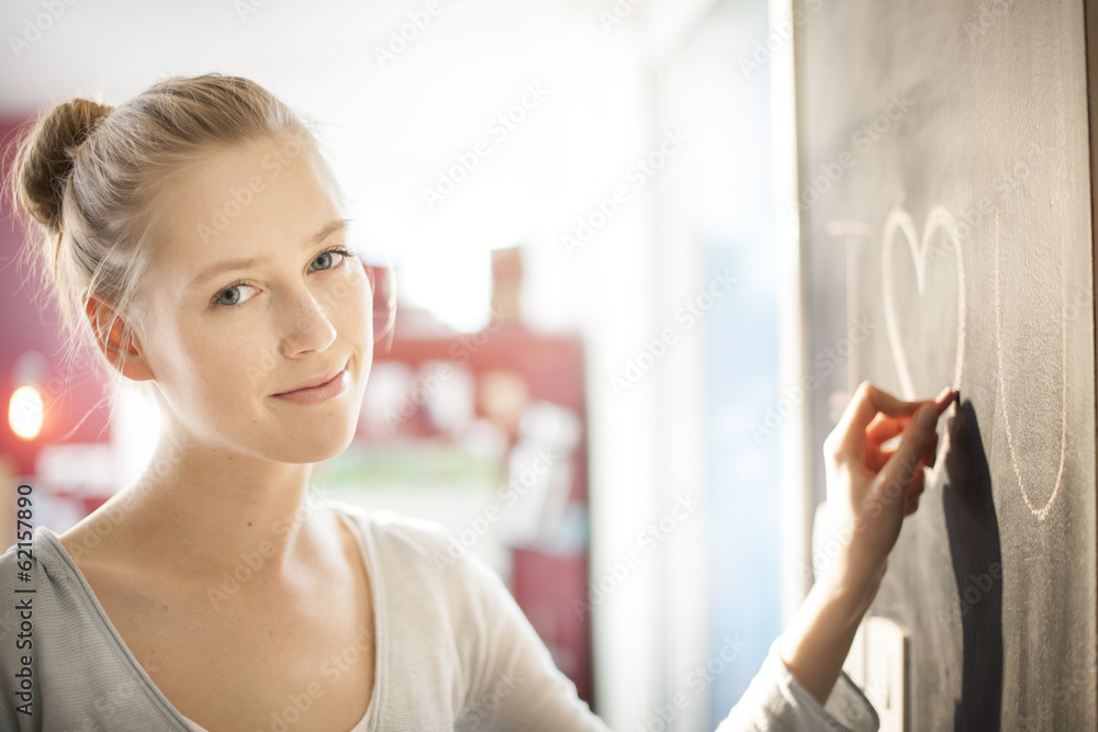beautiful young woman drawing a love message on a blackboard at