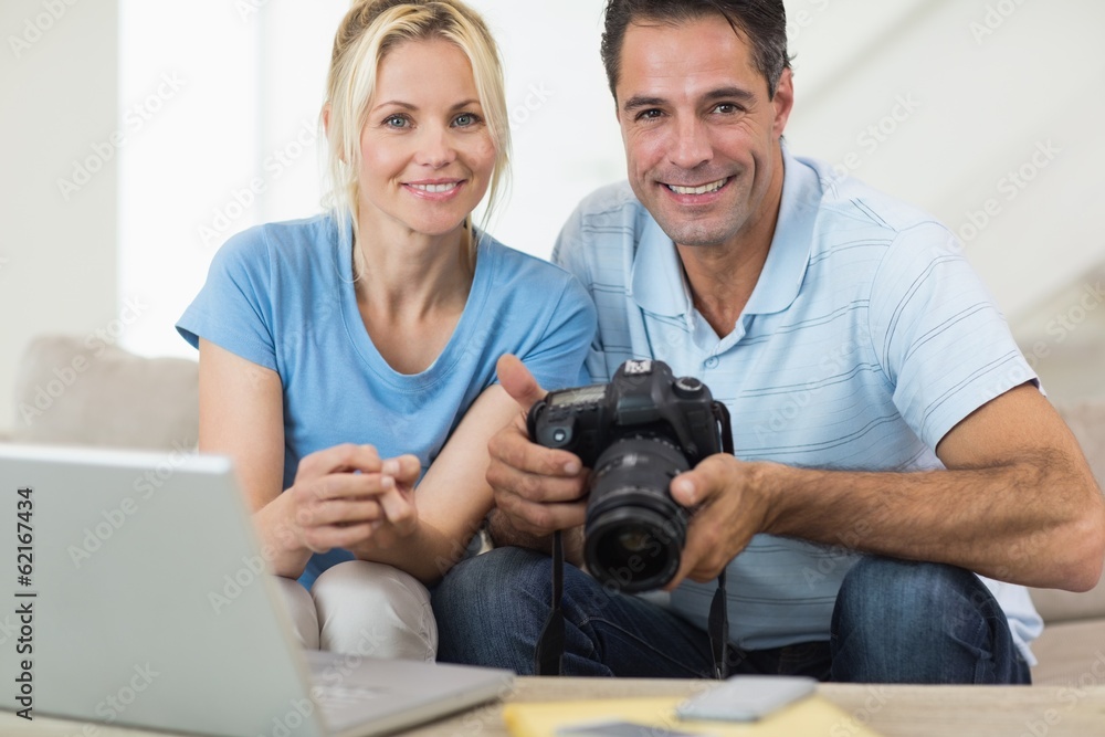 Happy couple with camera and laptop on sofa in living room Happy couple with camera and laptop on sofa in living room