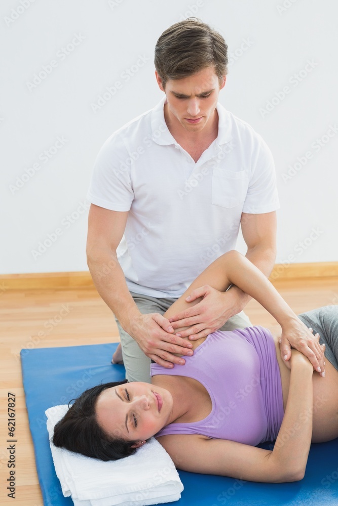 Masseur moving pregnant womans shoulder on a mat Masseur moving pregnant womans shoulder on a mat
