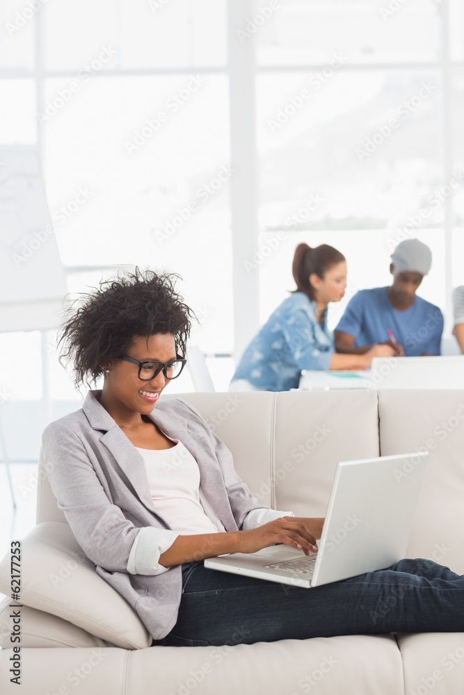 Woman using laptop with colleagues in background at creative Woman using laptop with colleagues in background at creative