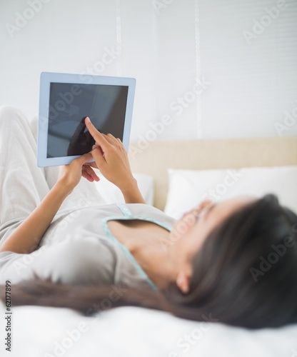Young girl lying on bed looking up at her tablet pc