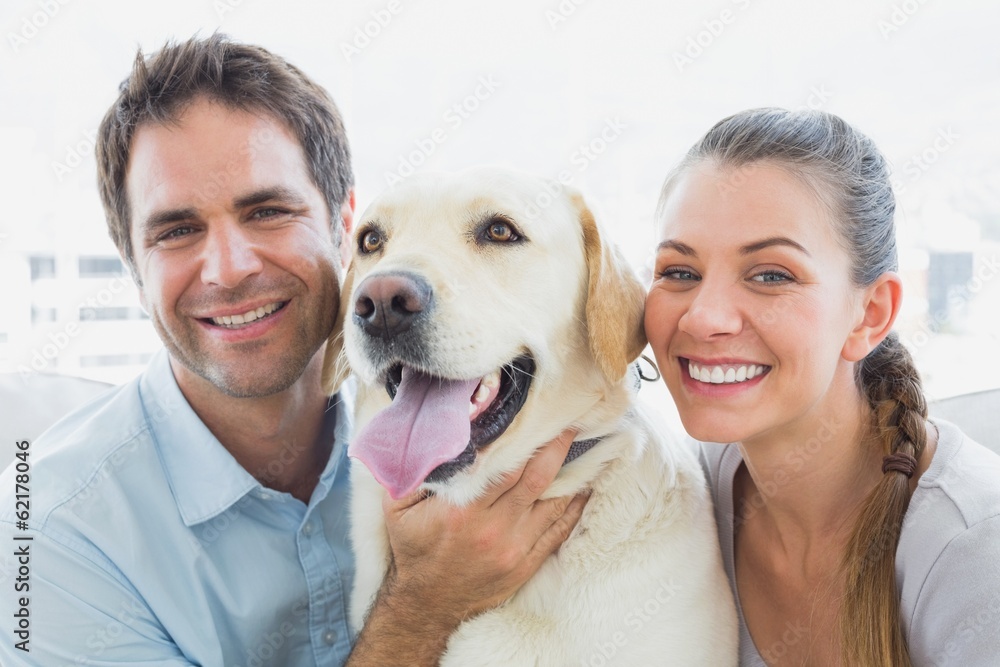 Happy couple rubbing their yellow labrador on the couch Happy couple rubbing their yellow labrador on the couch