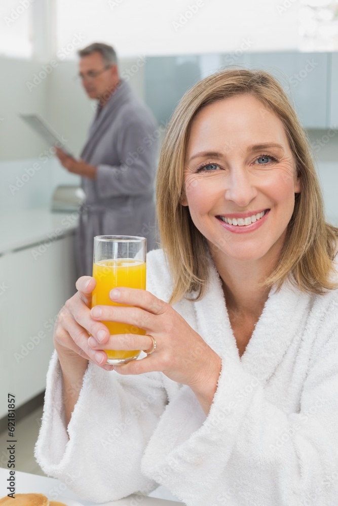 Smiling woman holding orange juice with man in background Smiling woman holding orange juice with man in background
