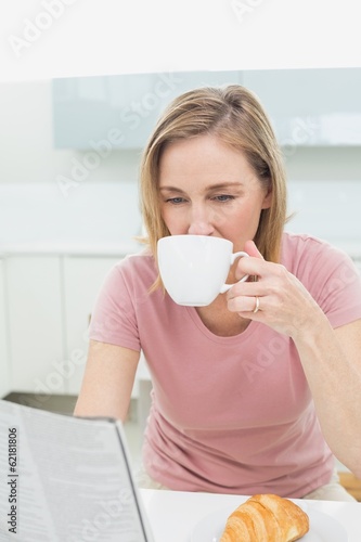 Woman reading newspaper while having coffee in kitchen