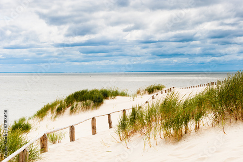 Fence on dune at seaside with stormy clouds visible.