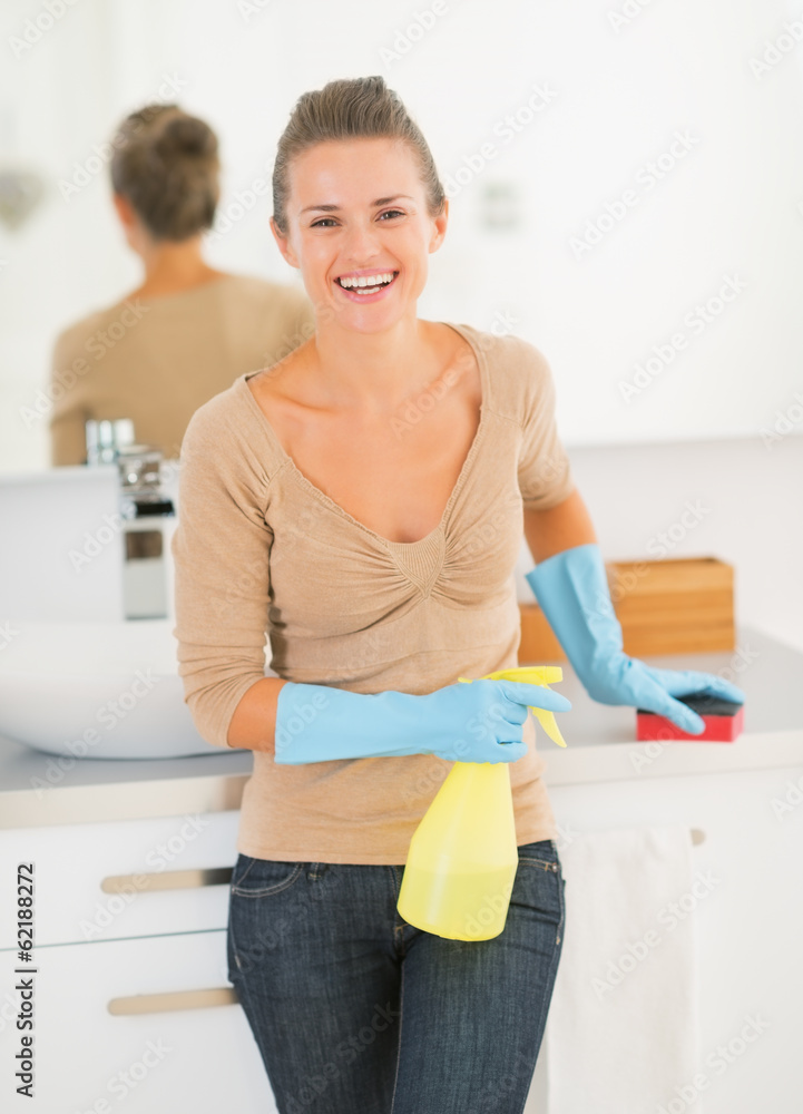 Portrait of happy housewife with spray bottle and sponge in bath Portrait of happy housewife with spray bottle and sponge in bath