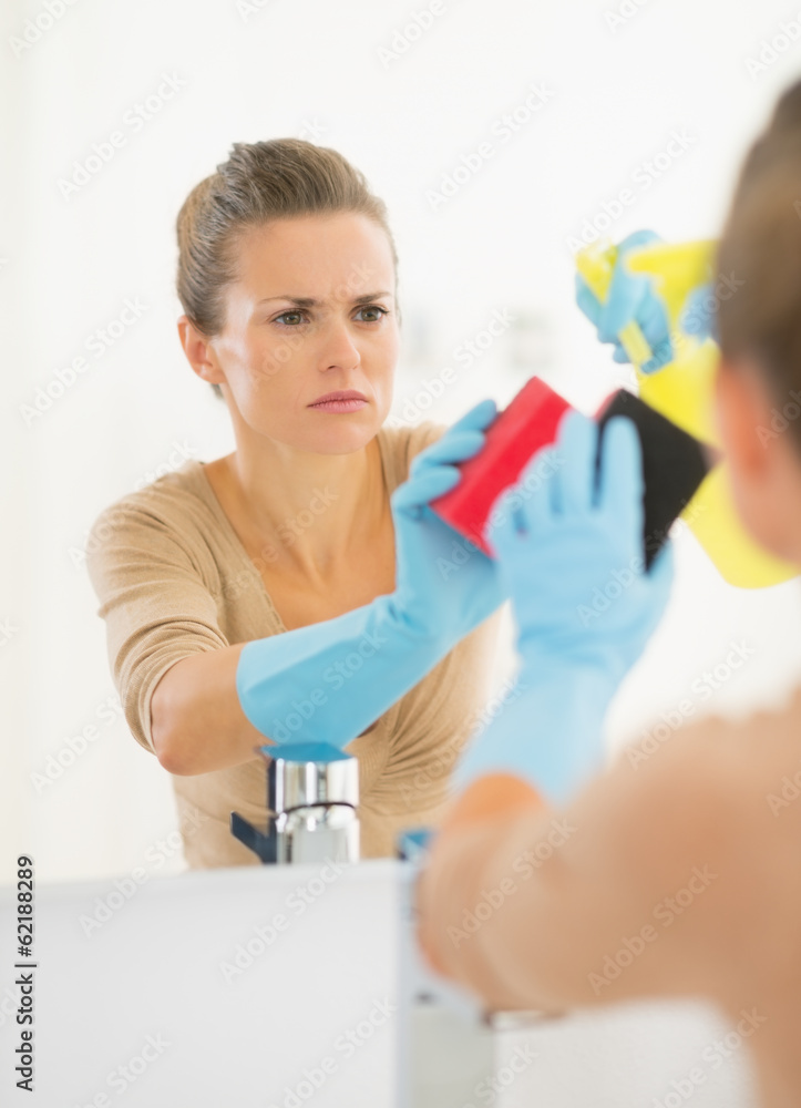 Young housewife cleaning mirror in bathroom Young housewife cleaning mirror in bathroom