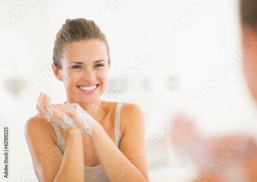 Portrait of happy young woman washing hands in bathroom