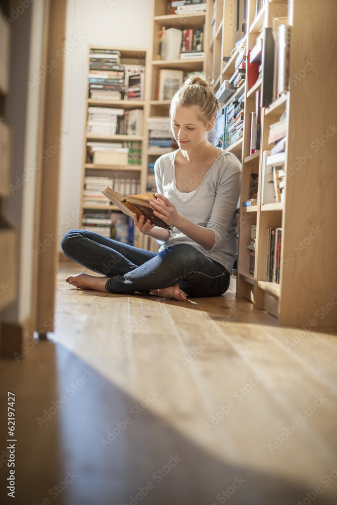 young woman sit on the floor reads a book near home library young woman sit on the floor reads a book near home library