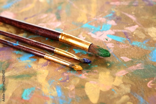 Many brushes in paints on multicolor wooden background