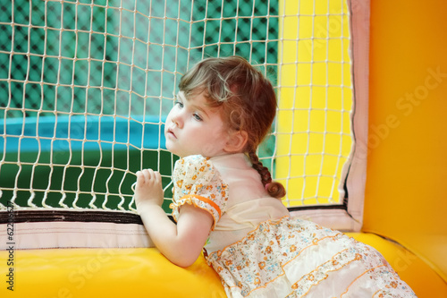 Little beautiful girl in dress stands in bouncy castle an