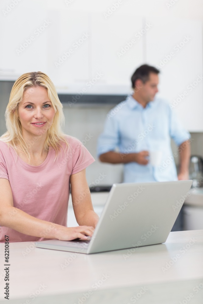 Woman using laptop with man drinking coffee in kitchen Woman using laptop with man drinking coffee in kitchen