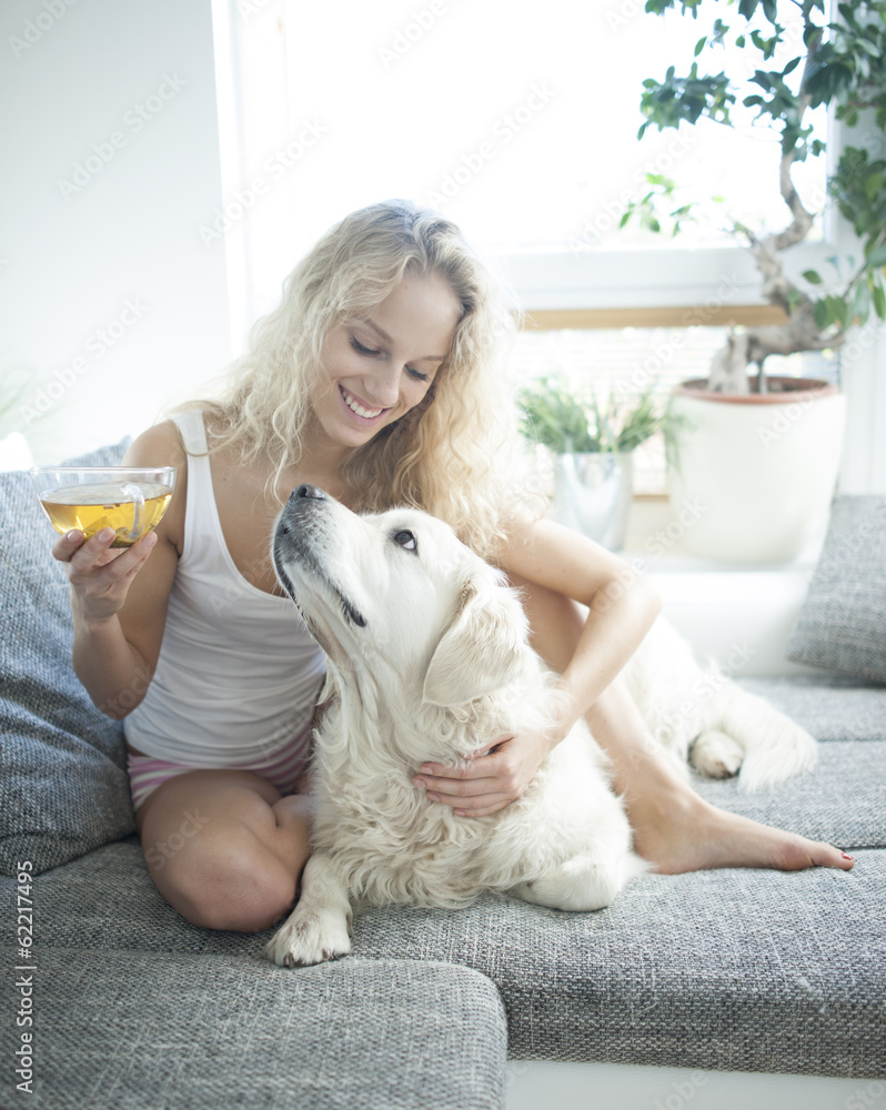 Beautiful woman holding tea cup while touching dog on sofa