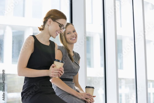 Happy businesswomen with disposable coffee cups at office Free Download Happy businesswomen with disposable coffee cups at office - GFXLoad