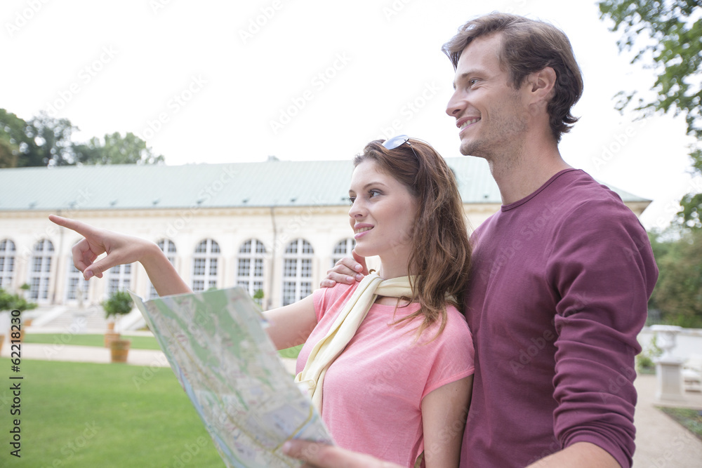 Woman with map showing something to man against building Woman with map showing something to man against building