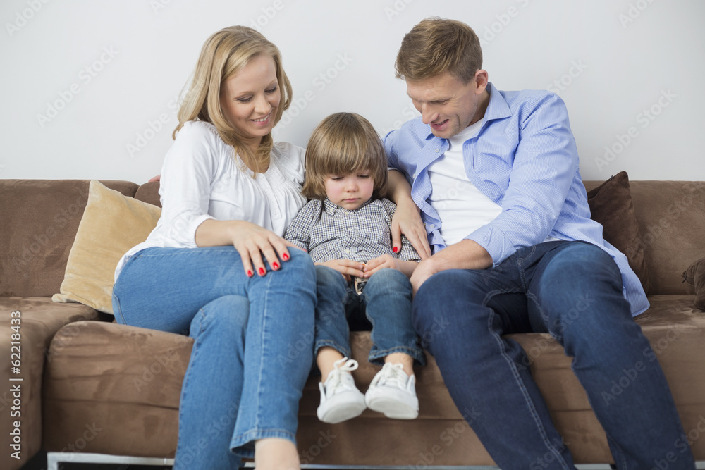 Parents sitting with sad son on sofa at home Parents sitting with sad son on sofa at home