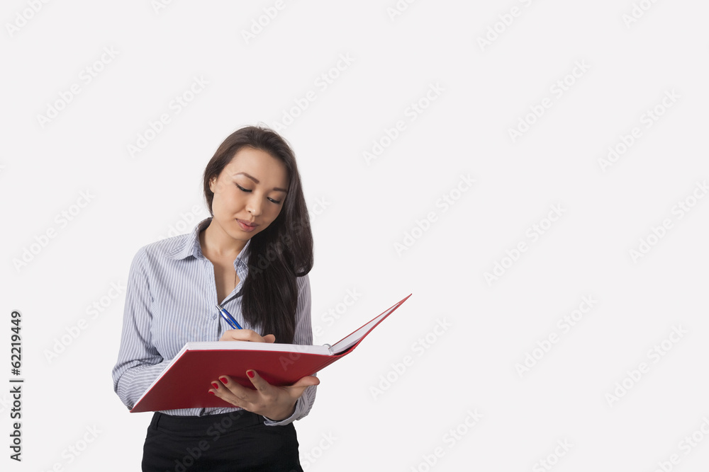 Businesswoman writing in book against gray background Businesswoman writing in book against gray background
