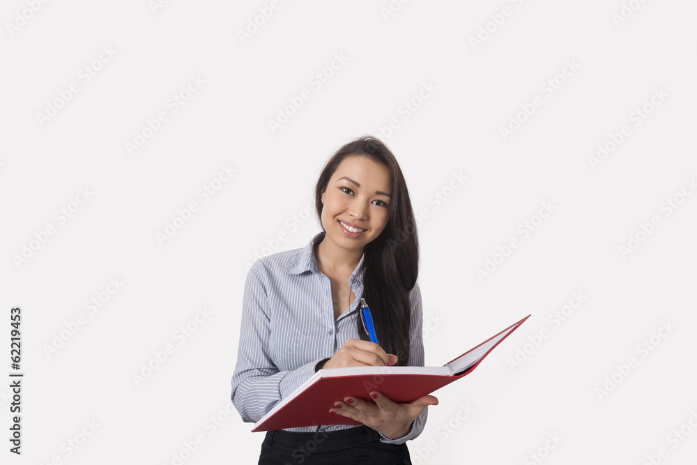 Businesswoman writing in book against gray background Businesswoman writing in book against gray background