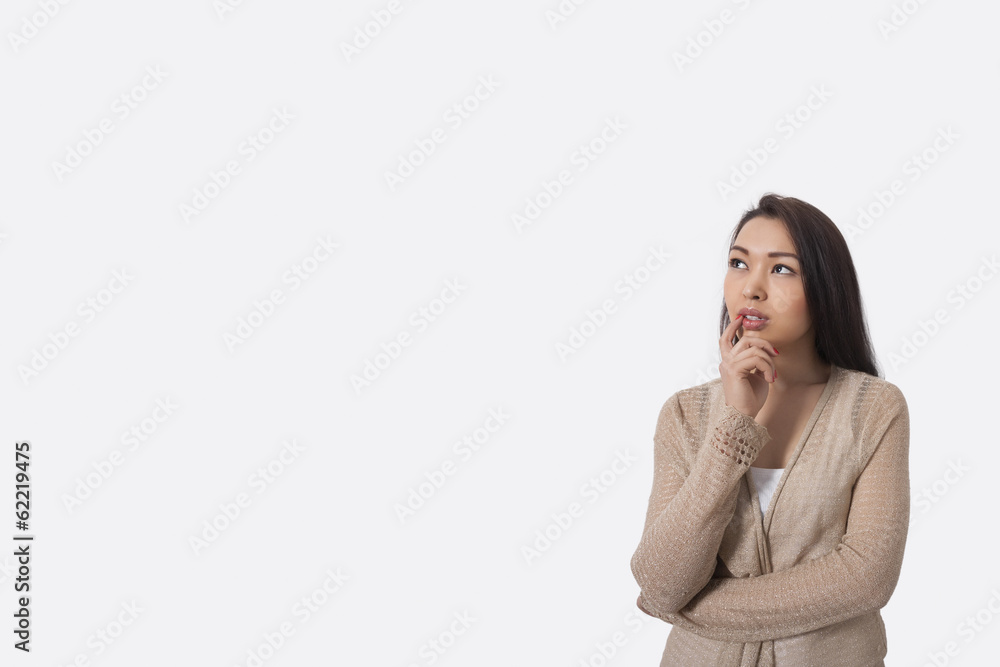 Thoughtful young woman standing against gray background Thoughtful young woman standing against gray background