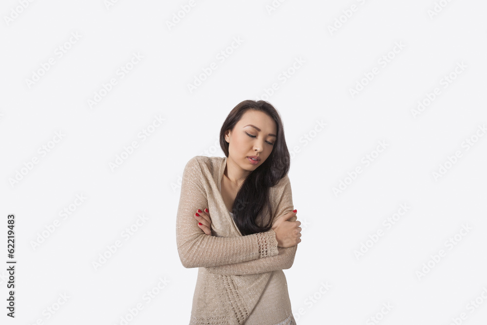 Young woman with arms crossed shivering against gray background Young woman with arms crossed shivering against gray background