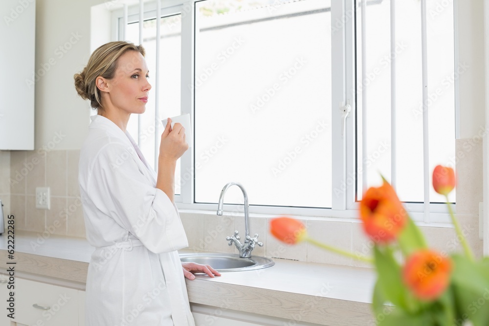 Thoughtful woman in bathrobe standing with coffee cup Thoughtful woman in bathrobe standing with coffee cup